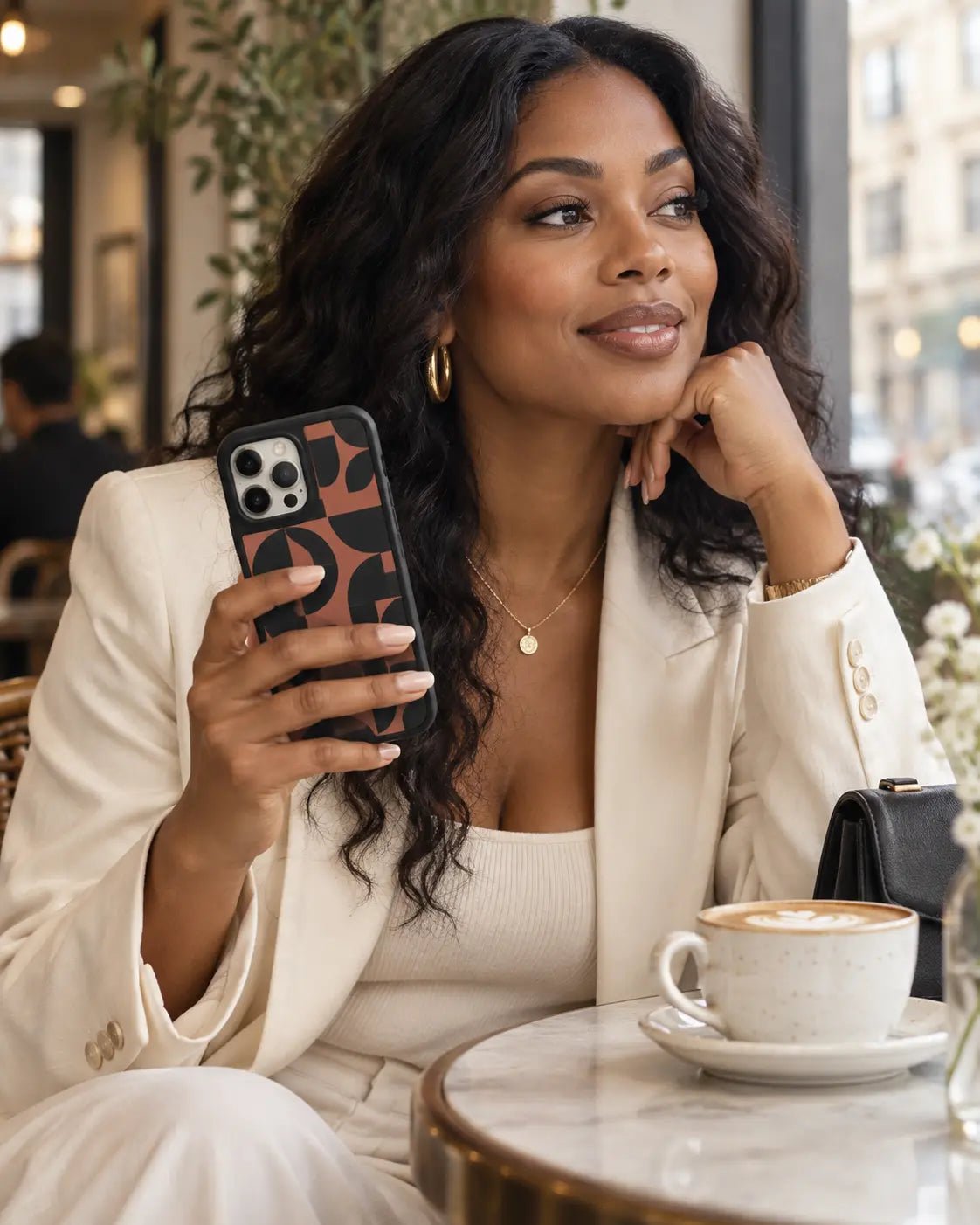 Woman at a cafe carrying a Black Bumper case with a terracotta geometric pattern